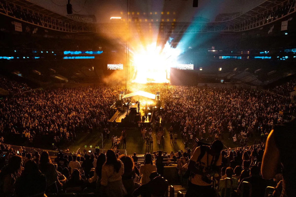 Grande público diante de palco iluminado em show de estádio, foto ilustrativa