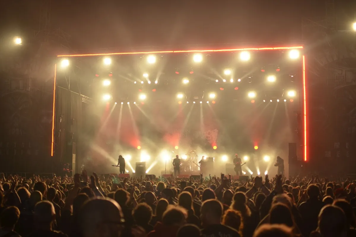 Banda em palco com luzes e fumaça diante de grande plateia à noite