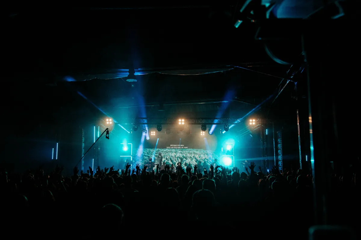 Músicos se apresentando em palco iluminado diante do público