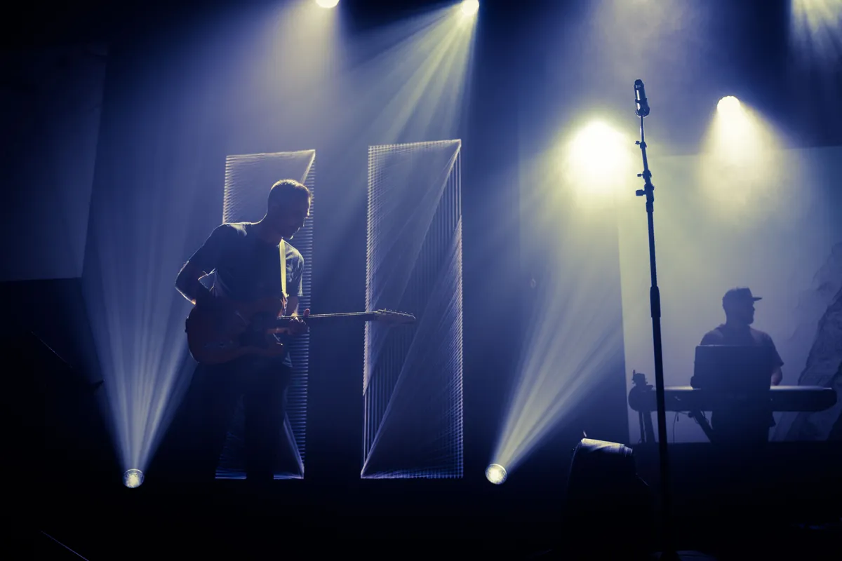 Músicos se apresentando em palco iluminado diante do público