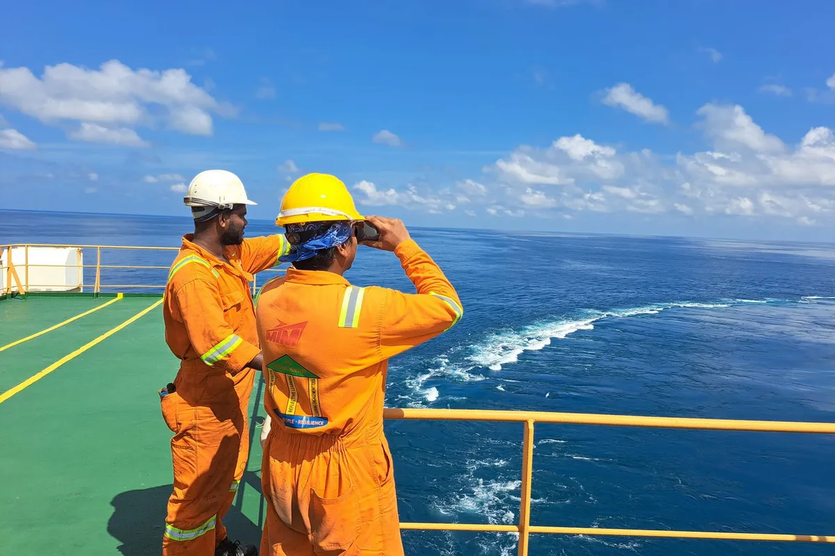 Tripulantes de uniforme laranja no convés de um navio